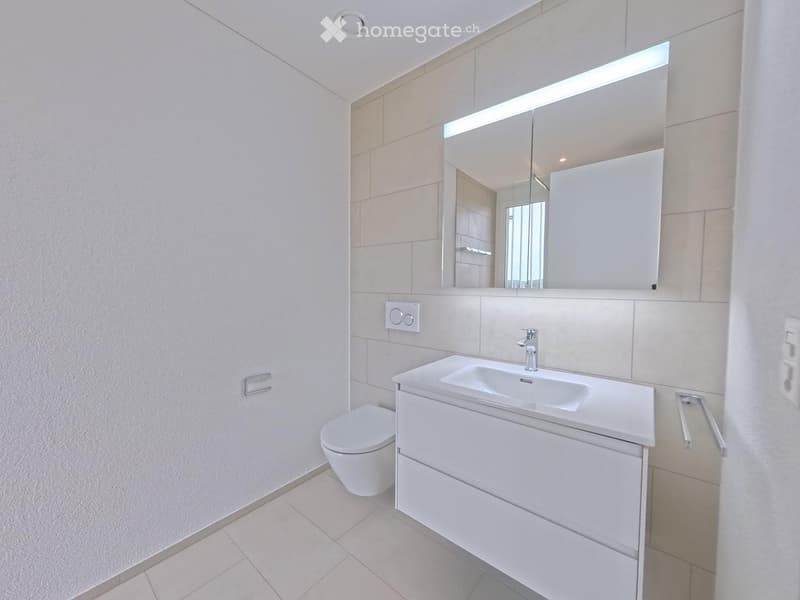 Modern bathroom with white tiles, a sink with a modern faucet, a toilet, and a large mirrored cabinet with built-in lighting.