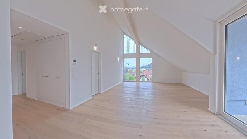Bright, empty attic room with wooden flooring, white walls, and large windows offering a scenic view.
