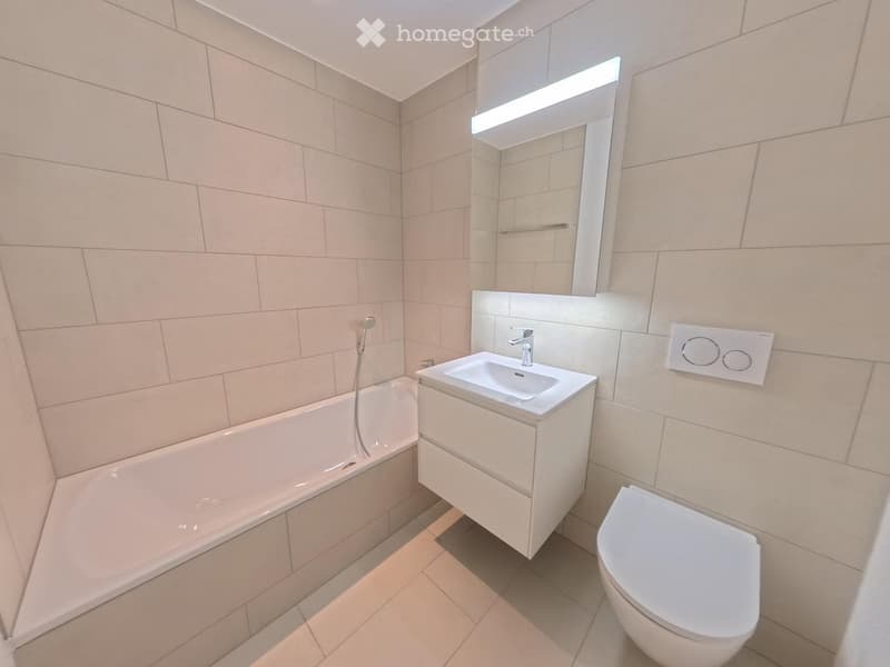 Modern bathroom with beige tiles, a bathtub, a sink with a mirror, and a toilet.