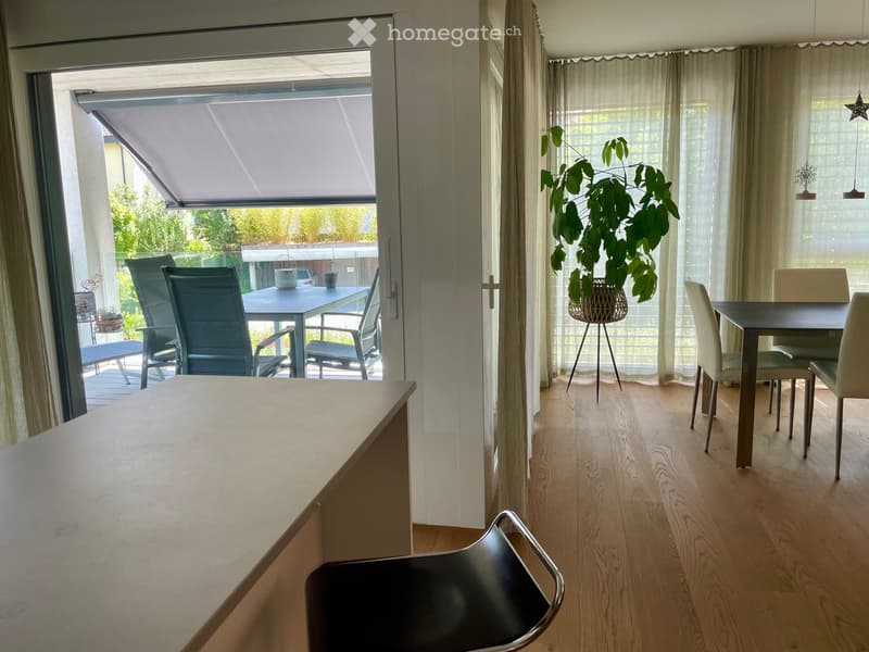 Modern dining area with light wooden flooring, a black dining table with white chairs, a potted plant, and a sliding glass door leading to a balcony with outdoor furniture.
