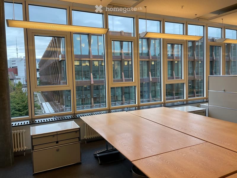 Modern office space with large windows, a long wooden conference table, and a metal cabinet.
