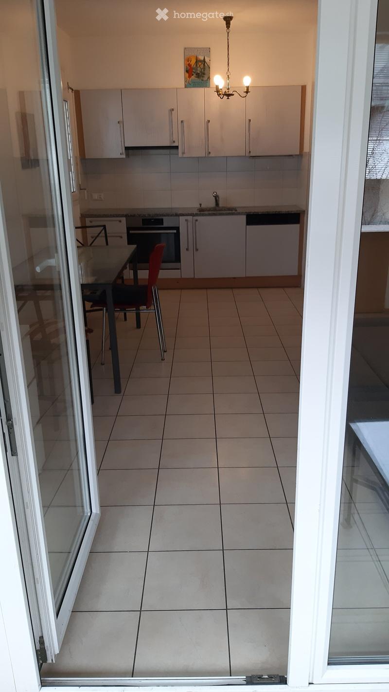 Modern kitchen with white cabinets, tiled floor, and a small dining area with a table and chair.
