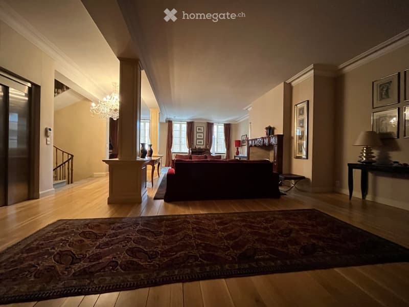 Elegant living room with wooden flooring, a large patterned rug, a red sofa, a chandelier, and several decorative items including vases and picture frames.