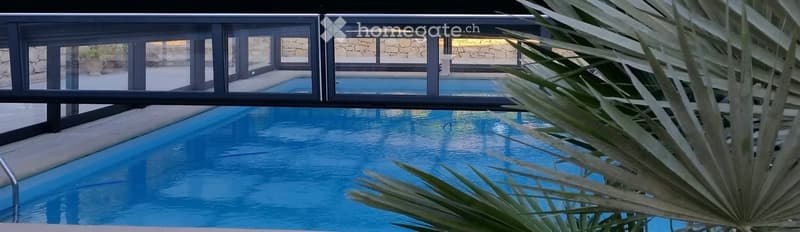 Outdoor swimming pool, covered by glass, surrounded by wall, trees