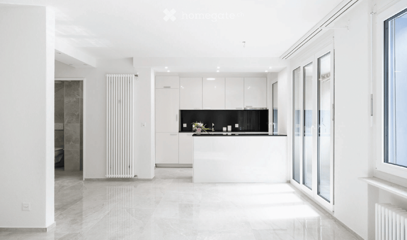 Modern, minimalist kitchen with white cabinets, a black countertop, and a sleek sink area. The space features large windows and a clean, open layout.