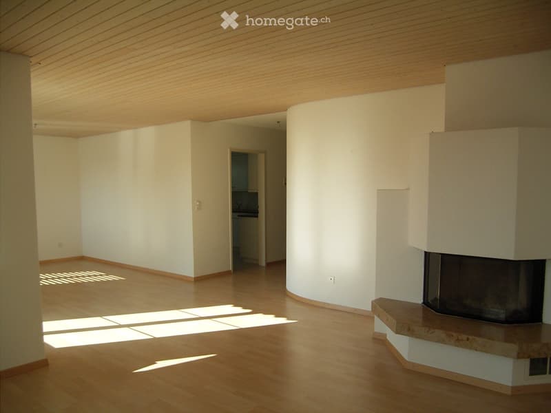 Empty living room with light wooden flooring, white walls, and a built-in fireplace. Sunlight streams in from a window, casting shadows on the floor.