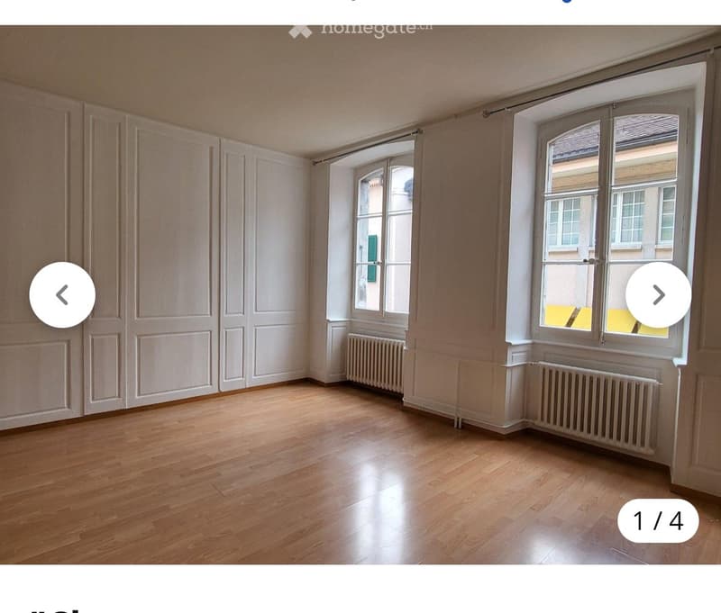 Empty room with wooden flooring, white walls, large windows, and radiators. No furniture or equipment present.