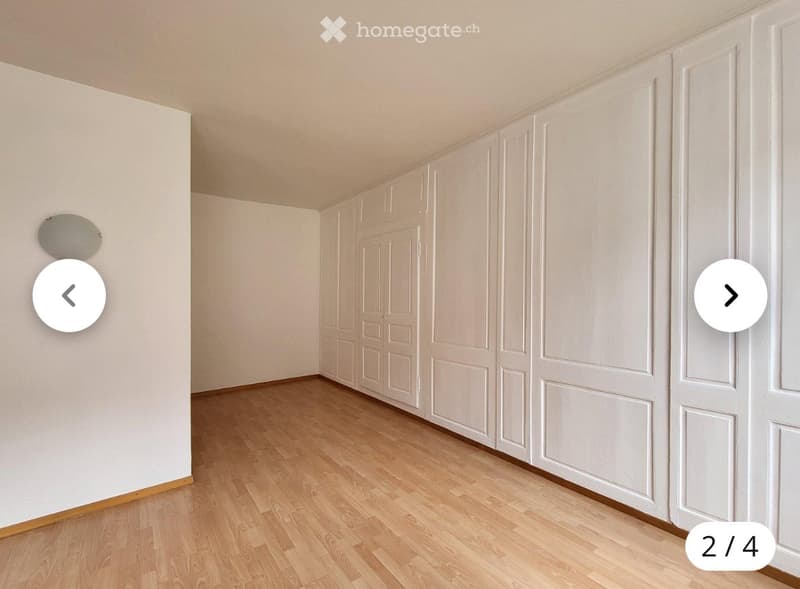 Empty room with light wooden flooring and white walls, featuring built-in white cabinetry along one wall.