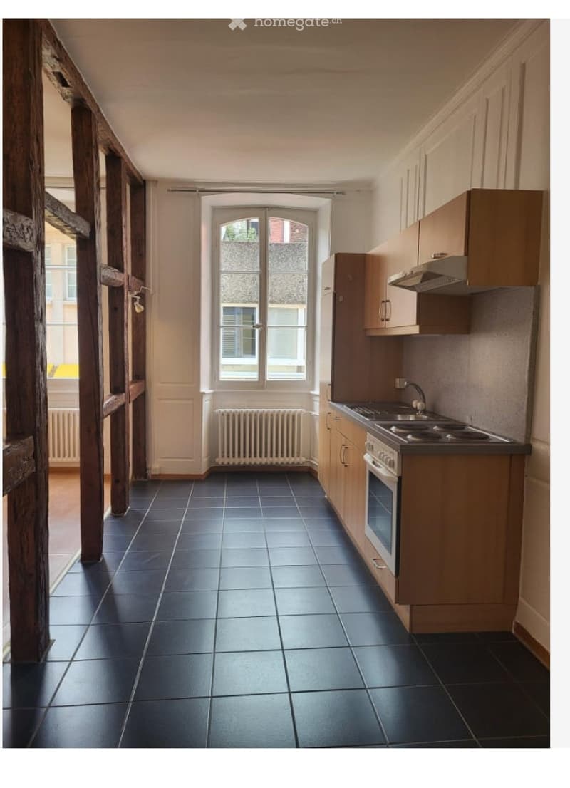 Modern kitchen with dark tiled floor, light wooden cabinets, built-in oven, sink, and radiator under window.