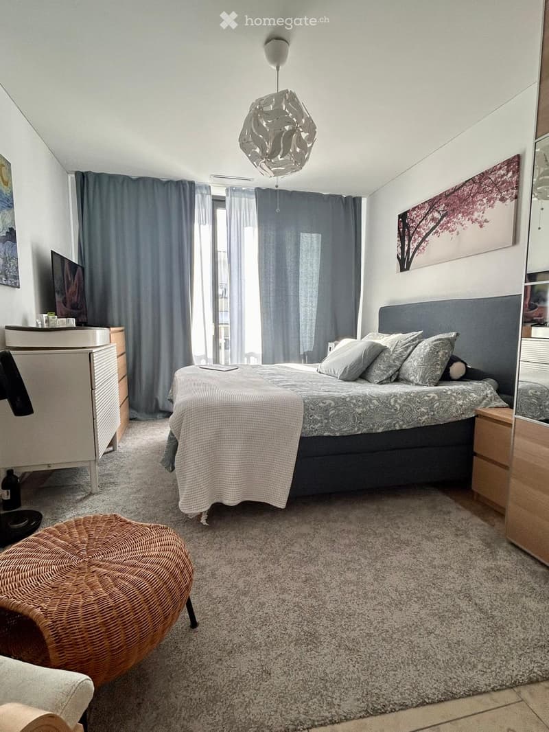 Modern bedroom with a large bed, nightstands, a round wicker stool, a mirror, a screen, and a painting on the wall.