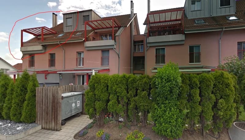 Garden area with trimmed hedges, a wooden fence, a small swimming pool, and a few flowering plants. The background shows a multi-story residential building with balconies and terraces.