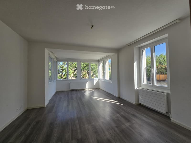 Empty room with wooden flooring, large windows, and radiators along the walls.