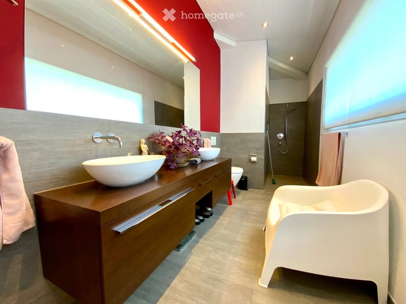 Modern bathroom with a wooden vanity, two sinks, a bathtub, and a shower area. Features include a large mirror, decorative plant, and sleek fixtures.