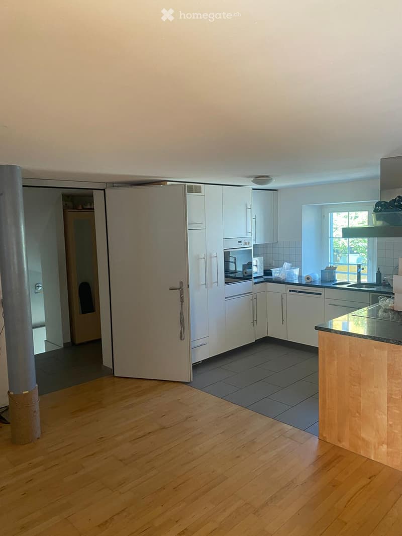 Modern kitchen with white cabinets, stainless steel appliances, and a wooden countertop island. The floor is wooden, and there is a window providing natural light.