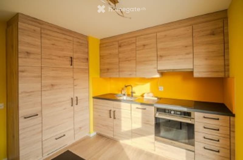 Modern kitchen with wooden cabinets, bright yellow walls, and stainless steel appliances including a sink, faucet, and oven.