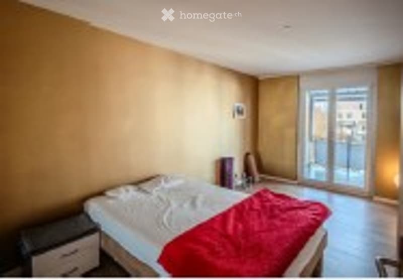 Bright bedroom with large windows and balcony access, featuring a neatly made bed, nightstand, and mirror.