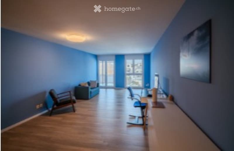 Bright, modern room with blue walls and wooden flooring. Features a sofa, chairs, a desk with a computer, and a table.