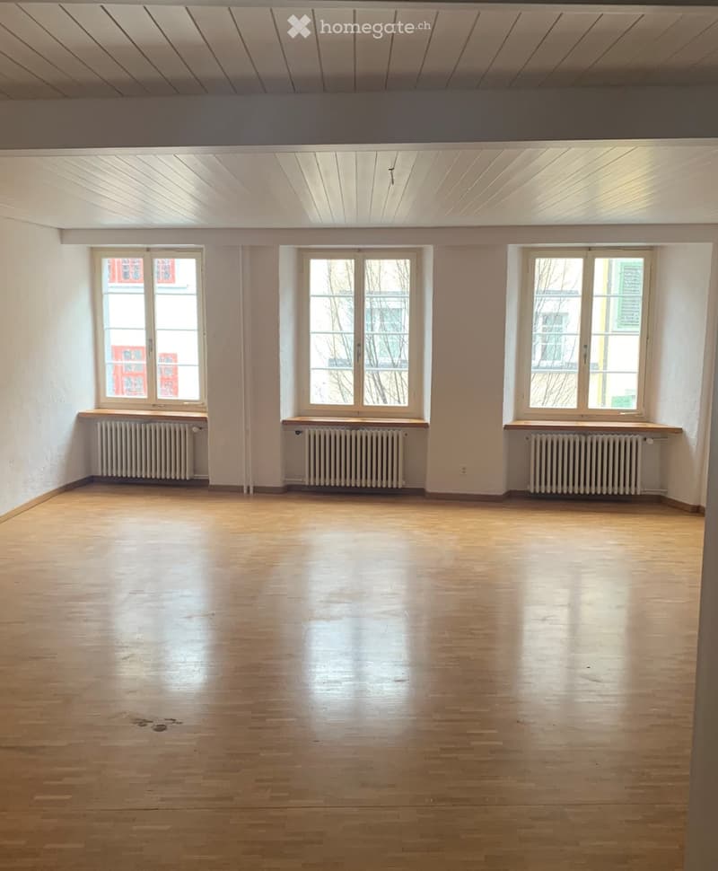 Empty room with wooden flooring, white walls, and three windows with radiators beneath them.
