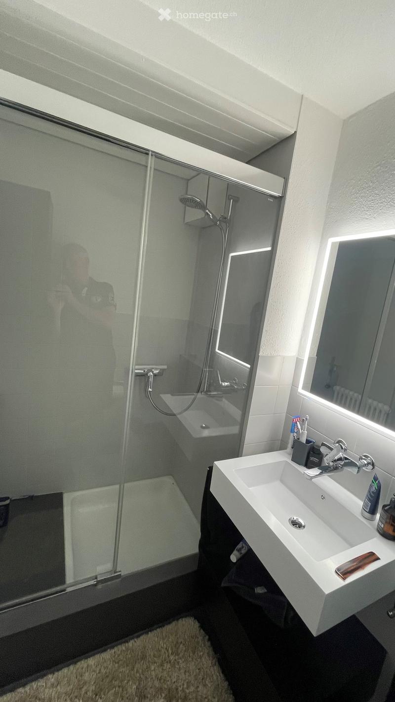Modern bathroom with a white sink, mirror, shower, and toiletries on the counter.