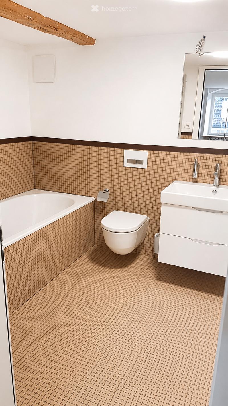 Modern bathroom with brown tiled walls and floor, white bathtub, toilet, sink, and mirror.
