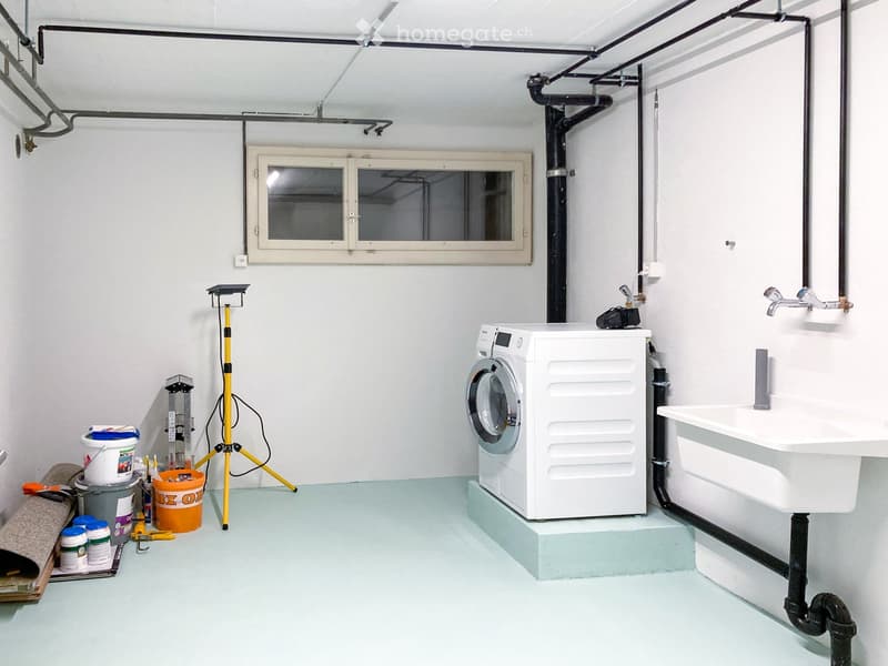 Utility bathroom with a washing machine, sink, and various tools and equipment.
