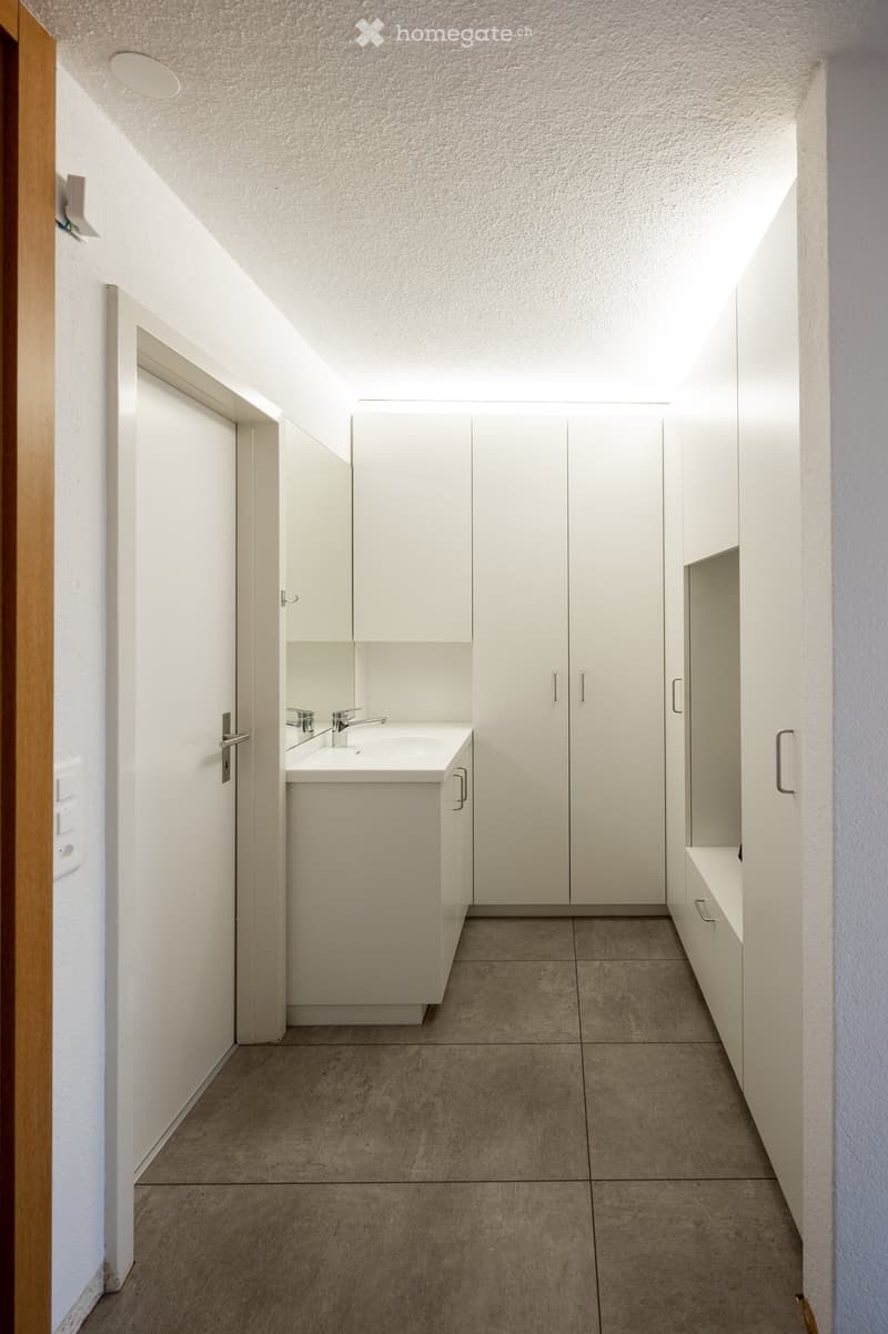 Modern bathroom with white cabinets, a sink, and a mirror. The space features a clean, minimalist design with a tiled floor and recessed lighting.