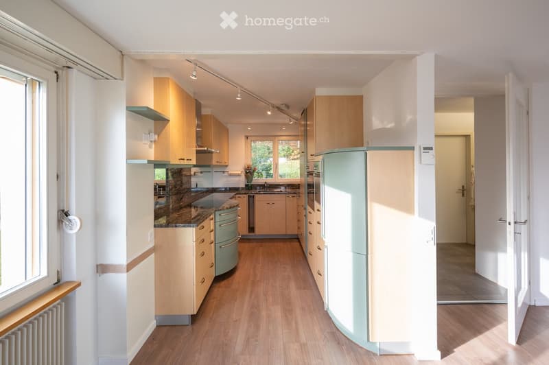 Modern kitchen with light wooden cabinets, granite countertops, stainless steel appliances, and a central island.