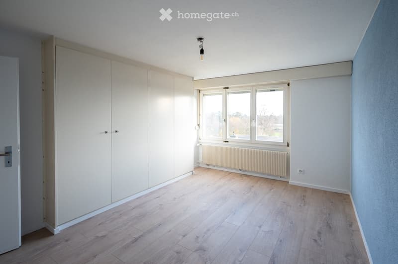 Empty room with light wooden flooring, white walls, large windows, and built-in wardrobes.