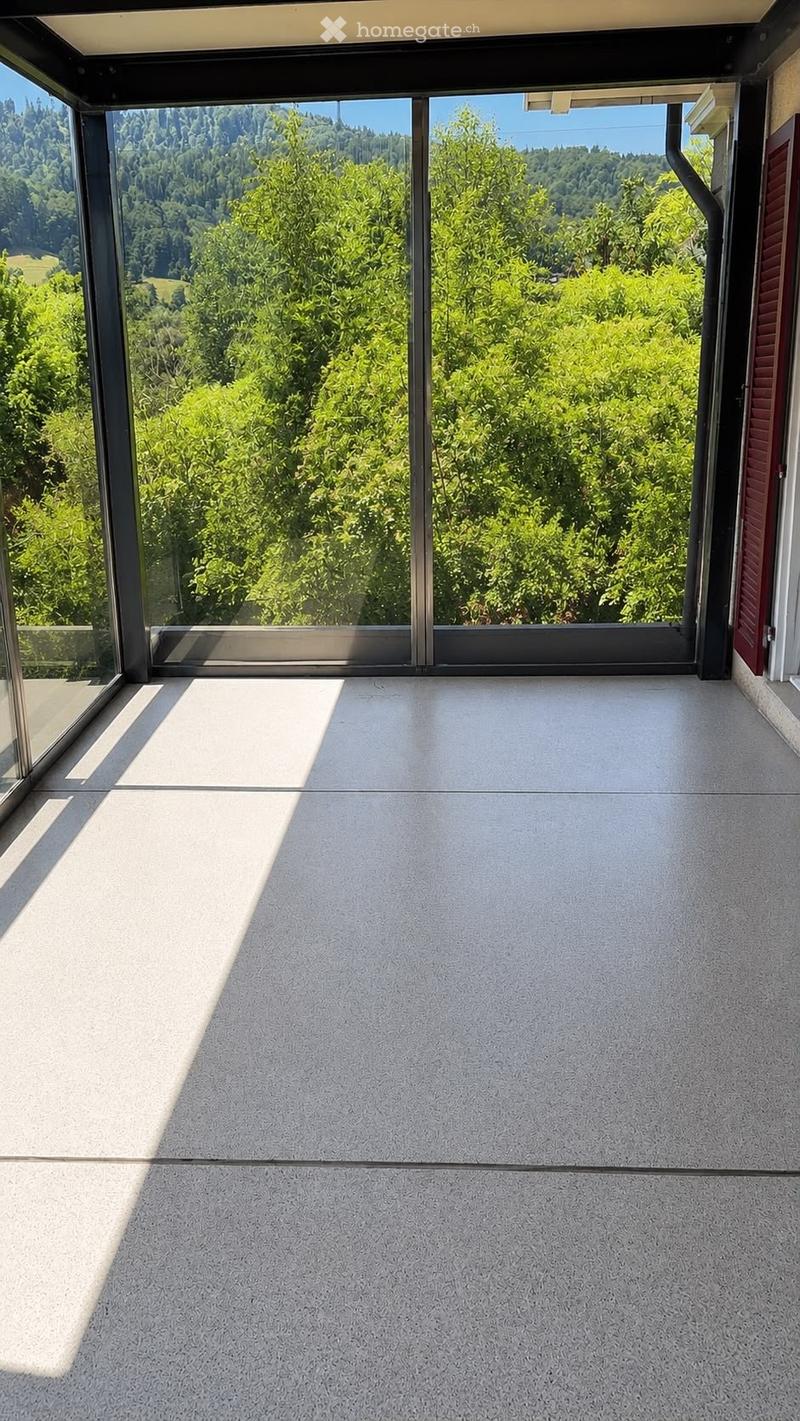Modern balcony with large glass sliding doors, concrete floor, and scenic view of green trees and hills.