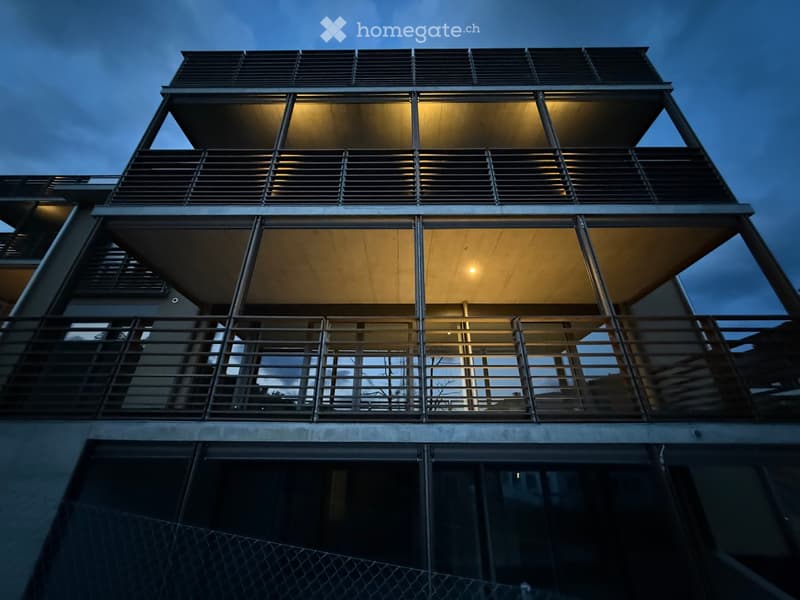 Modern building, large balcony with railings, multiple levels, yellow lighting on the balconies