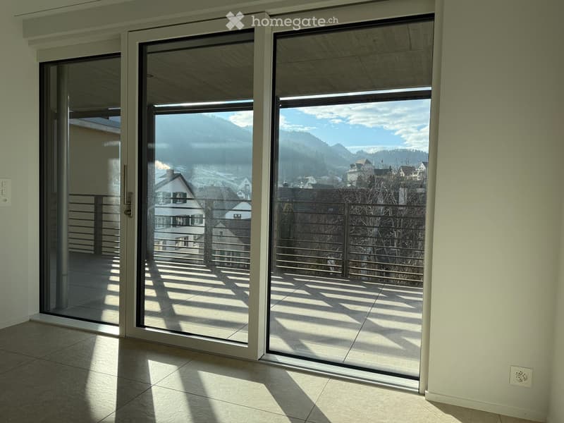 Empty room with large glass sliding doors leading to a balcony with mountain view
