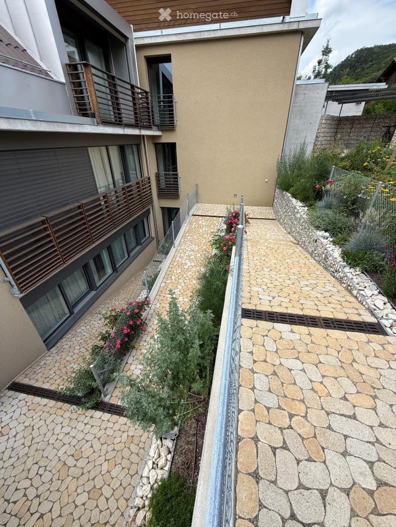 A modern building with balconies and a landscaped garden area featuring stone pathways, small plants, and flowers.