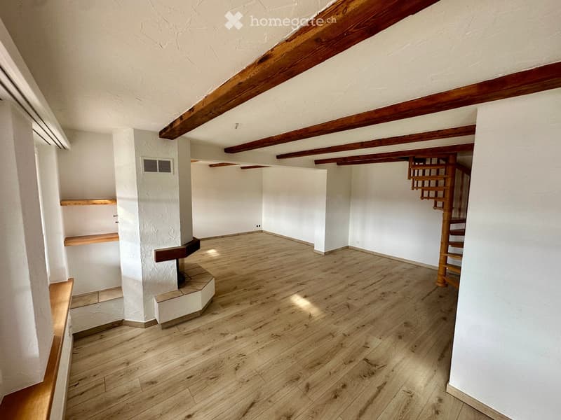Empty room with wooden flooring, white walls, exposed wooden beams, and a small staircase leading to an upper level.