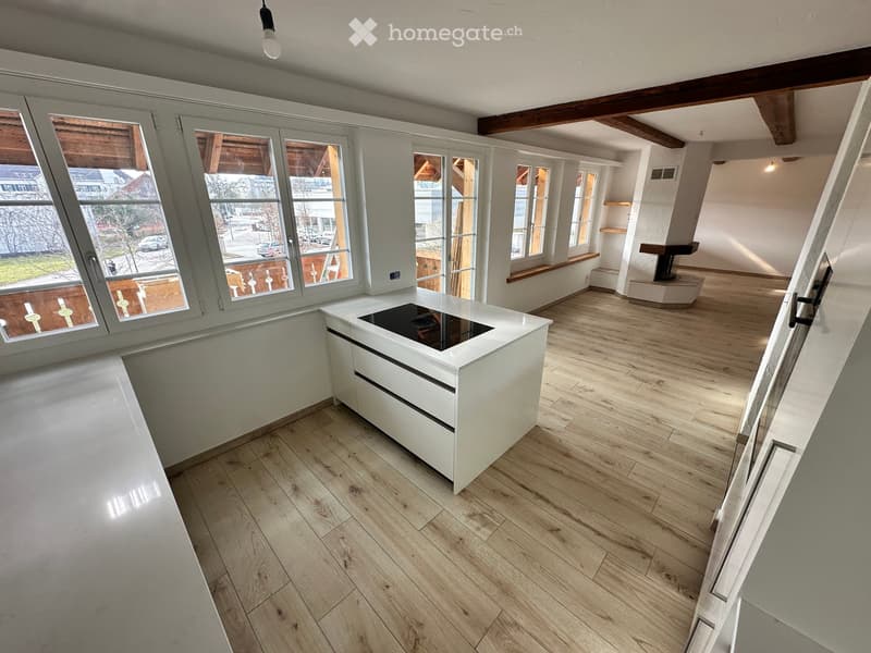 Modern kitchen with white cabinetry, wooden flooring, large windows, and an island with an induction cooktop.
