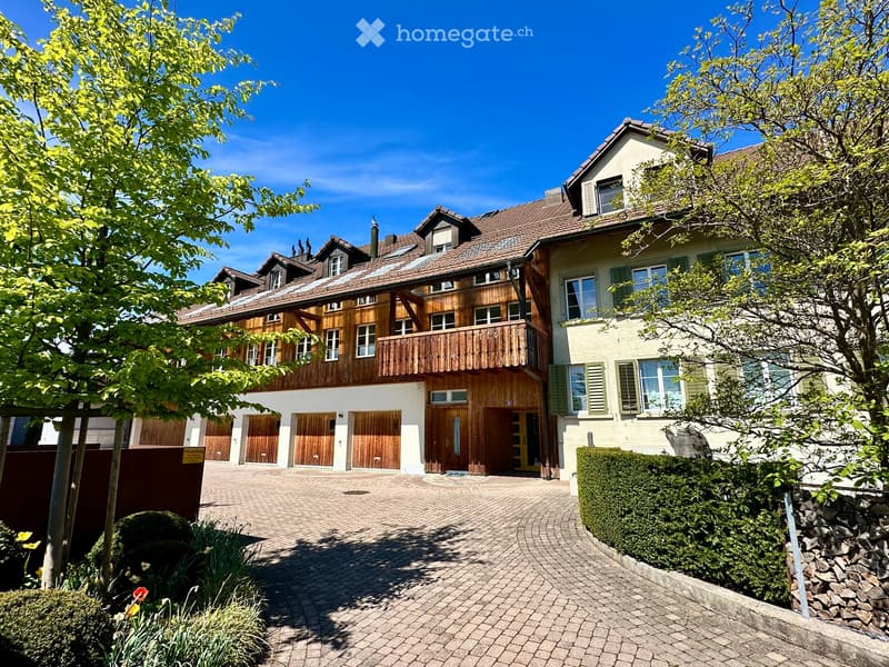 Two-story house with wooden balconies, multiple garage doors, and a well-maintained garden area.
