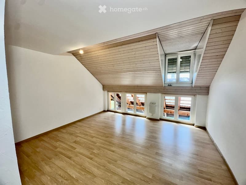 Empty attic room with wooden flooring, white walls, and large windows, including a skylight and a door leading to a balcony.