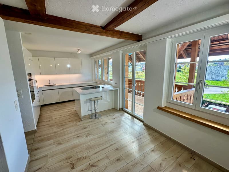 Modern kitchen with white cabinets, wooden flooring, island with bar stool, and large windows overlooking a balcony.