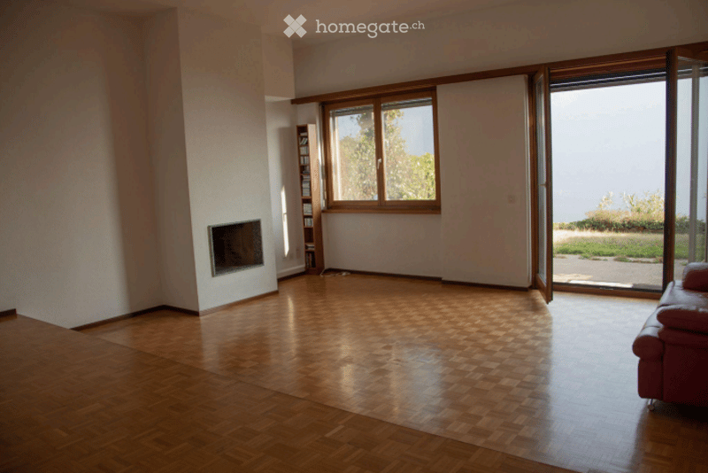 Bright living room with wooden parquet flooring, fireplace, large windows, and a red leather sofa.
