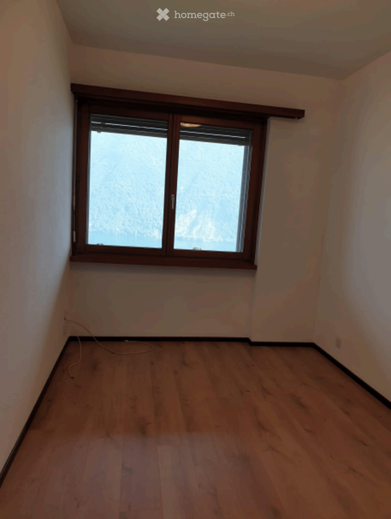 Empty room with wooden flooring and a large window with wooden frame, showing a view of the outdoors.