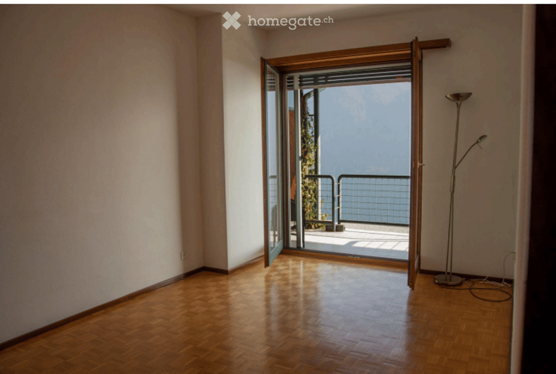 Empty room with wooden flooring, large open sliding doors leading to a balcony with a scenic view.