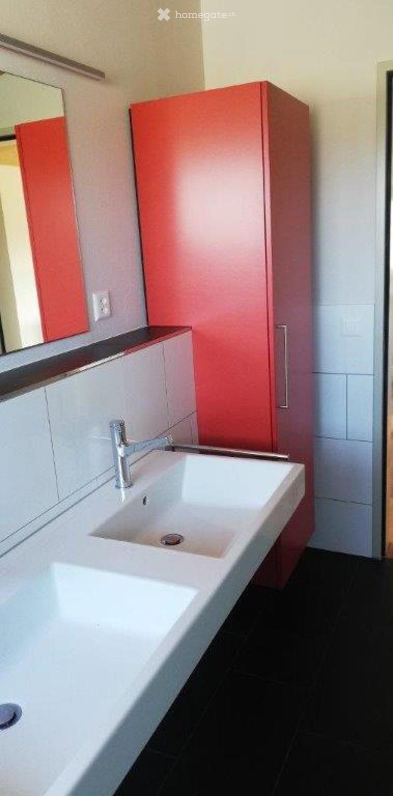 Modern bathroom with a white sink, chrome faucet, red cabinet, and a mirror above the sink.