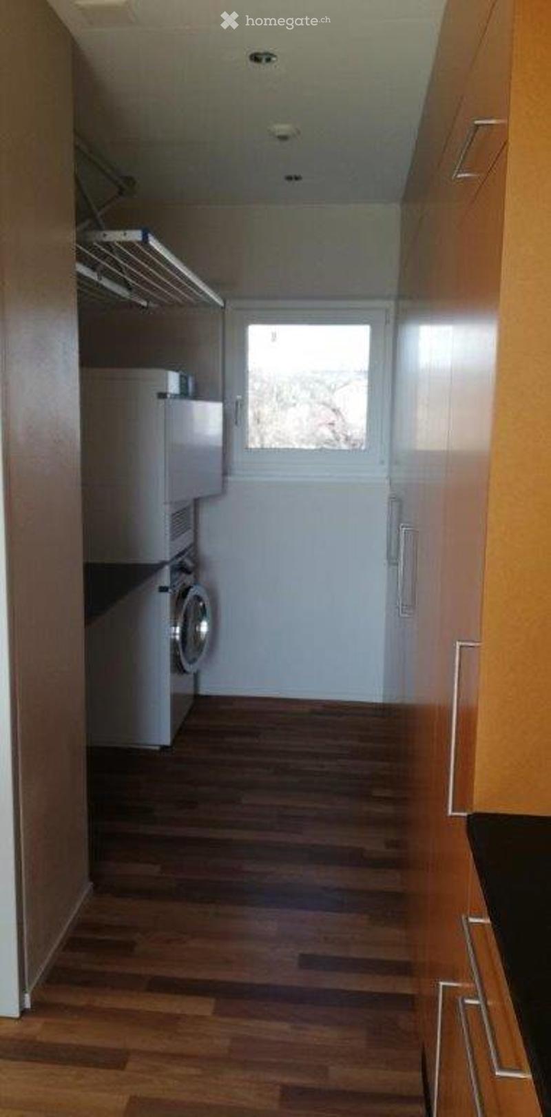 Hallway with wooden flooring, white walls, a window, and a private washing machine in the corner.