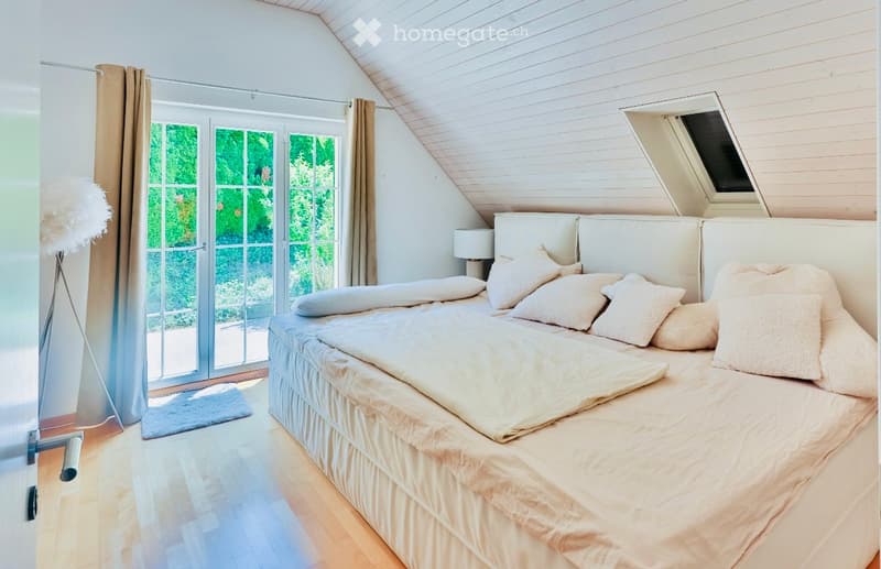 bedroom with a double bed, several pillows, white walls, hardwood floor, large sliding glass doors, a skylight, view of greenery