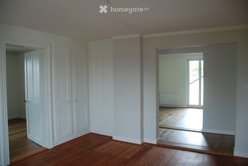 Empty room with wooden flooring, white walls, and multiple doors leading to other spaces.