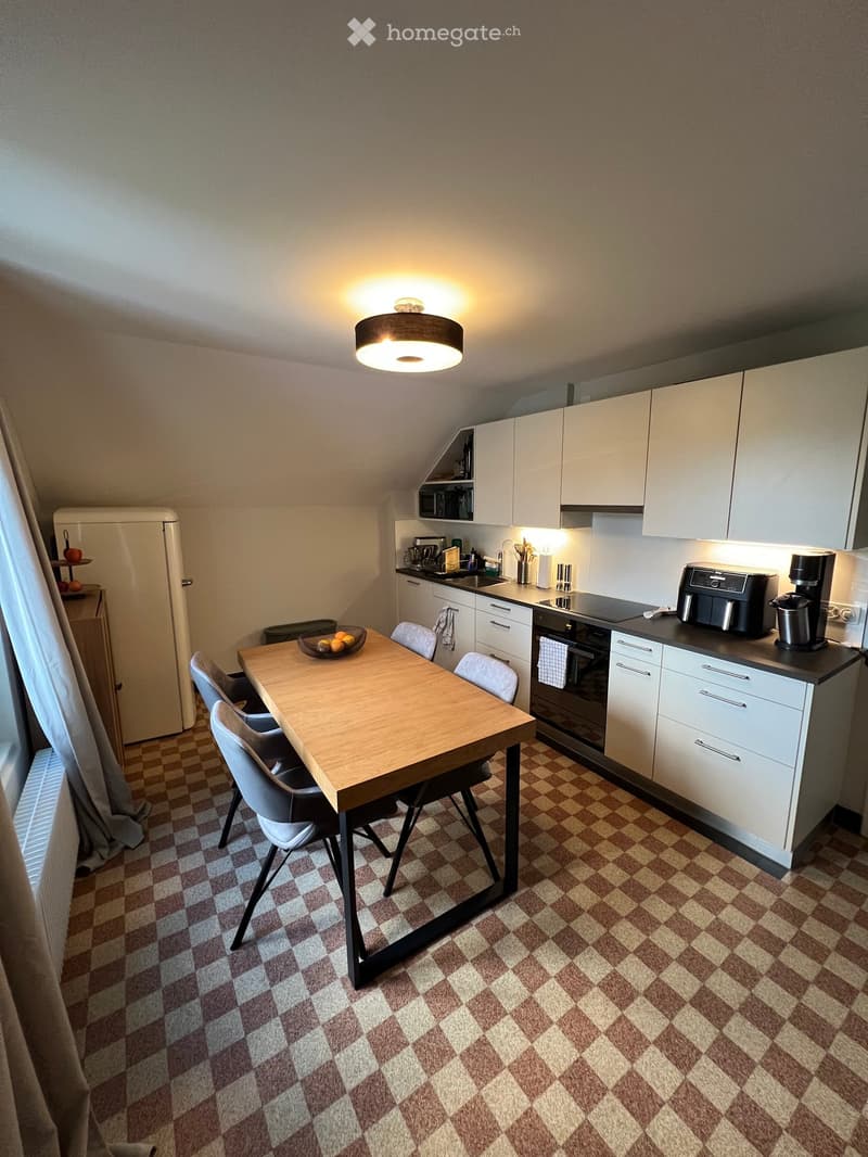 Modern kitchen with white cabinets, stainless steel appliances, a wooden dining table with four chairs, and a bowl of fruit on the table.