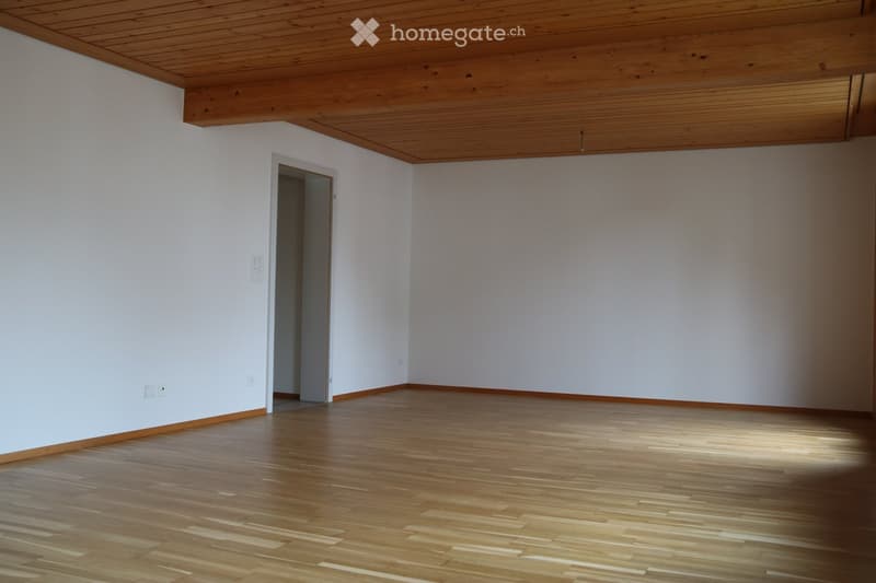 Empty room with light wooden flooring, white walls, and a wooden slanted ceiling. There is a doorway leading to another space.