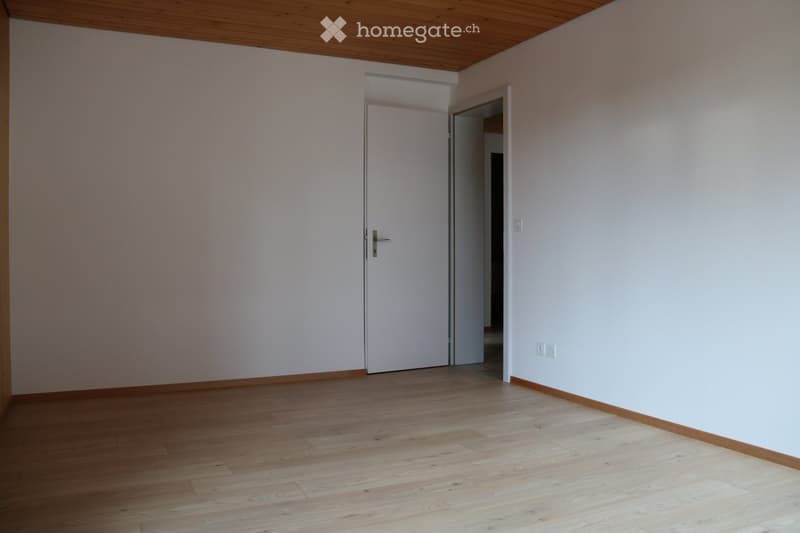 Empty room with light-colored walls, wooden flooring, and a closed white door leading to another space.