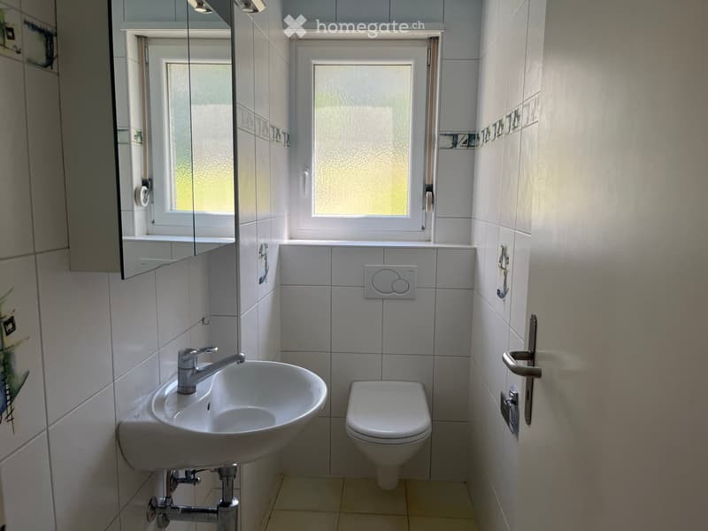 Modern bathroom with white tiles, a sink with a chrome faucet, a toilet, a mirror, and a cabinet.