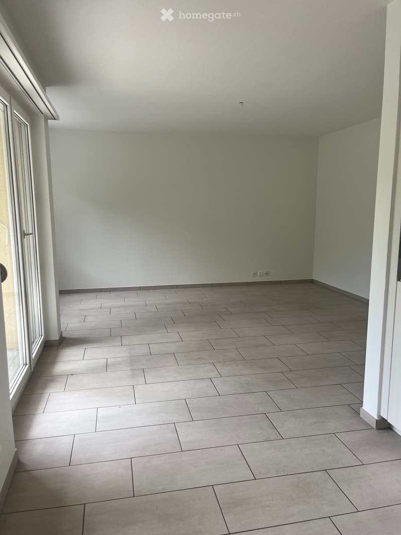 Empty room with tiled floor and white walls, featuring a large window and a door leading outside.