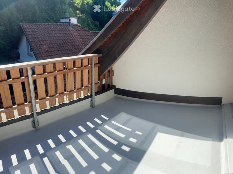 Roof terrace with wooden railing, white concrete floor, and a view of neighboring houses and greenery.